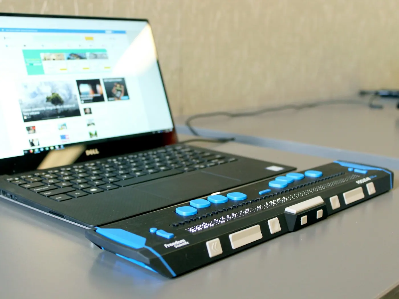 A laptop on a desk with a refreshable braille display in front of its keyboard