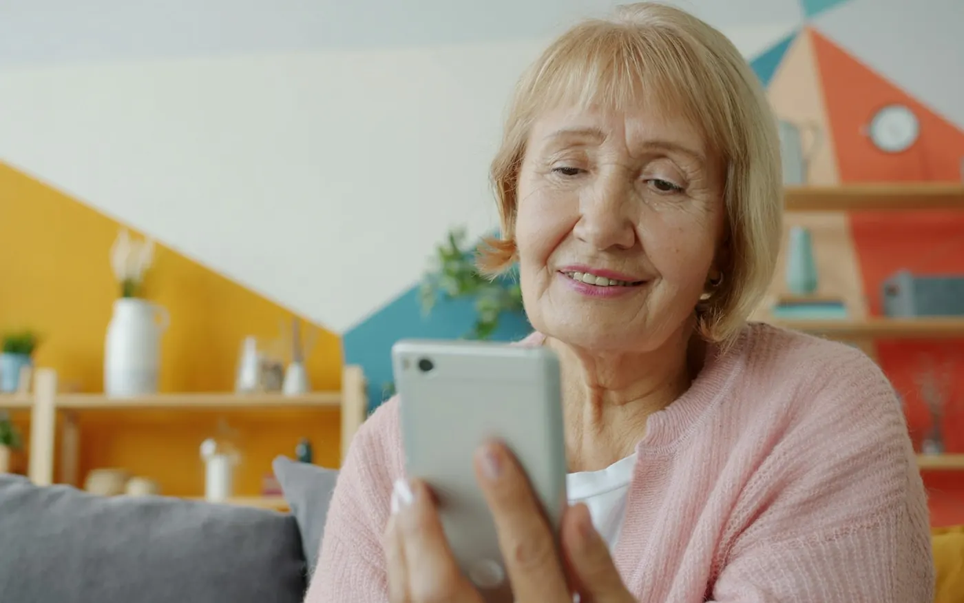 An older woman smiling as she reads her smartphone at home